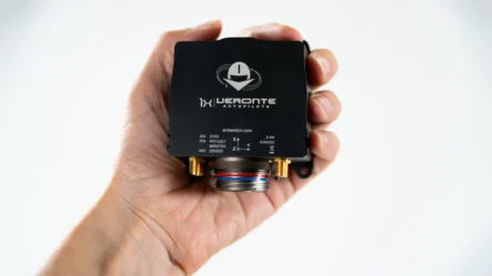 Hand holding a Veronte autopilot 1x 4.12 for drones and eVTOLs, a compact black device with connection ports and technical specifications visible on the front